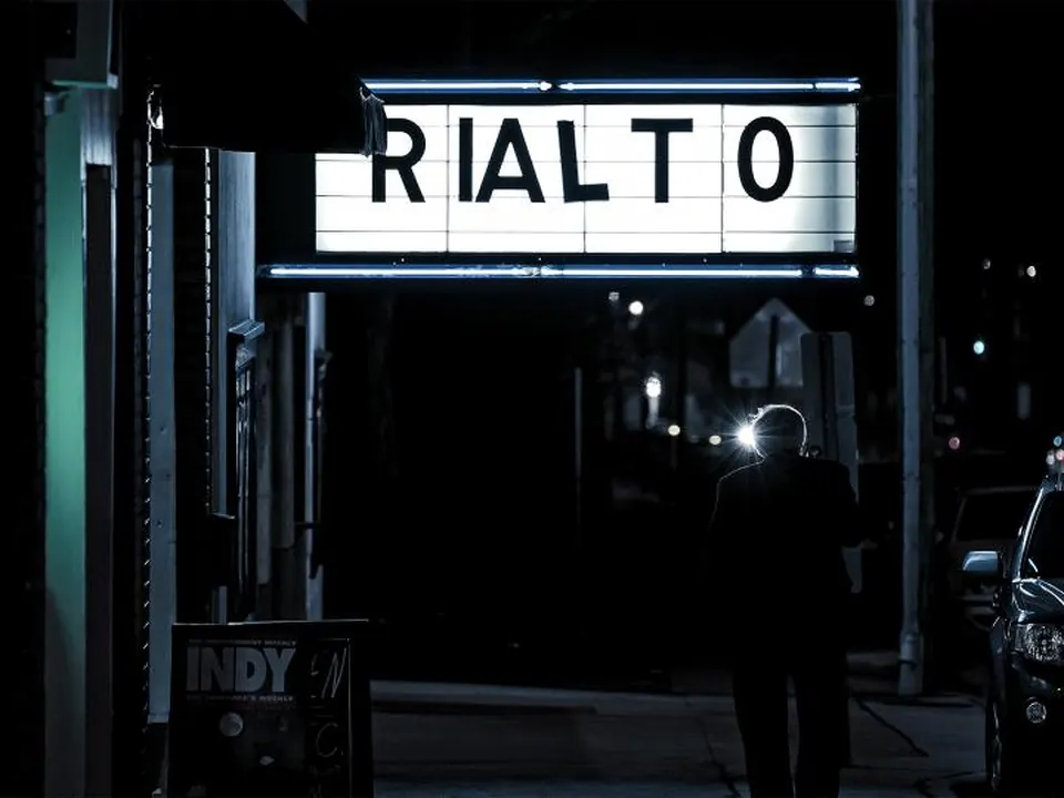 Brightly lit theater marquee glowing over the sidewalk at night