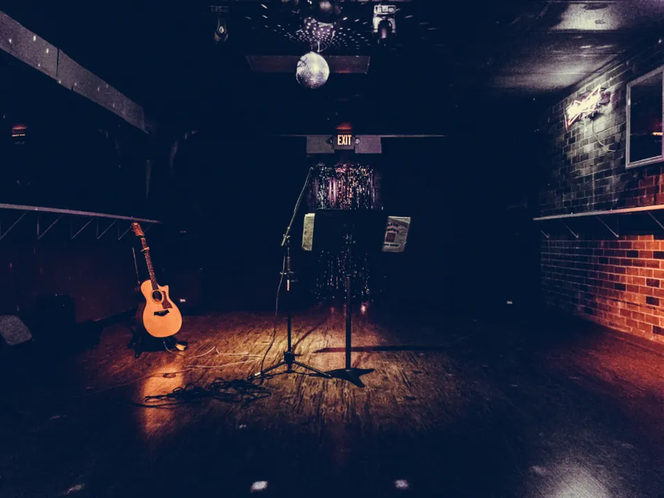 Empty comedy club stage with a brick wall backdrop, a wooden stool, and a microphone under a spotlight