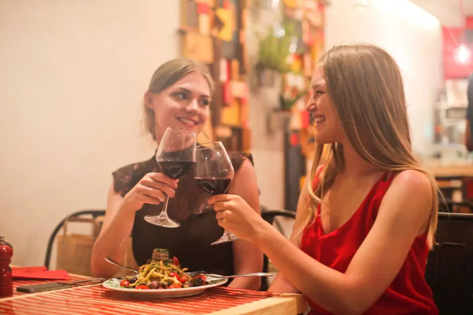 Two friends toasting red wine at a dinner table on a night out