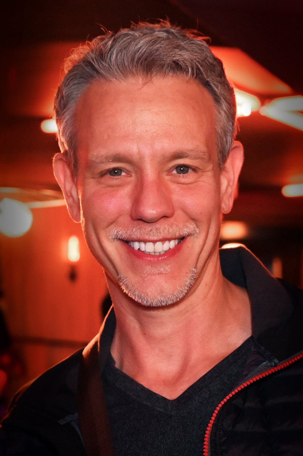 Adam Pascal smiling in a warmly lit room, 2024