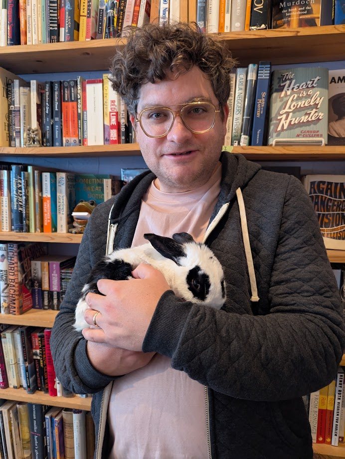 Comedian Alex Falcone holding a rabbit in Nat's Uptown Books, Minneapolis