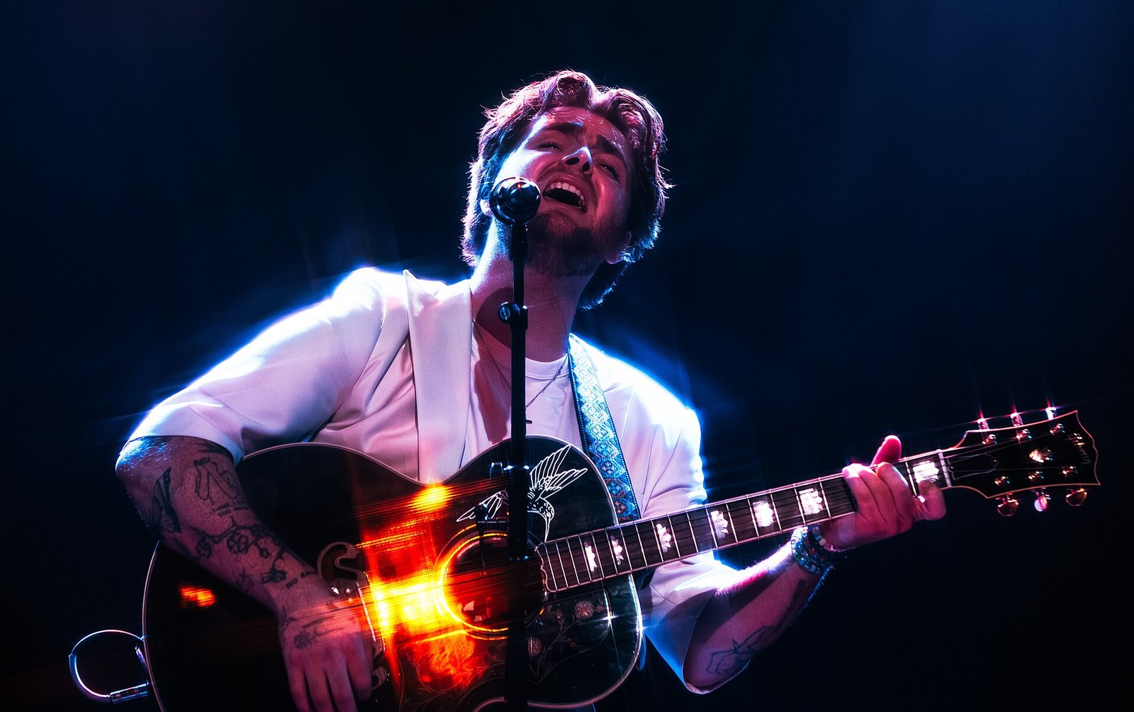 Alex Warren singing and playing acoustic guitar on stage, 2023
