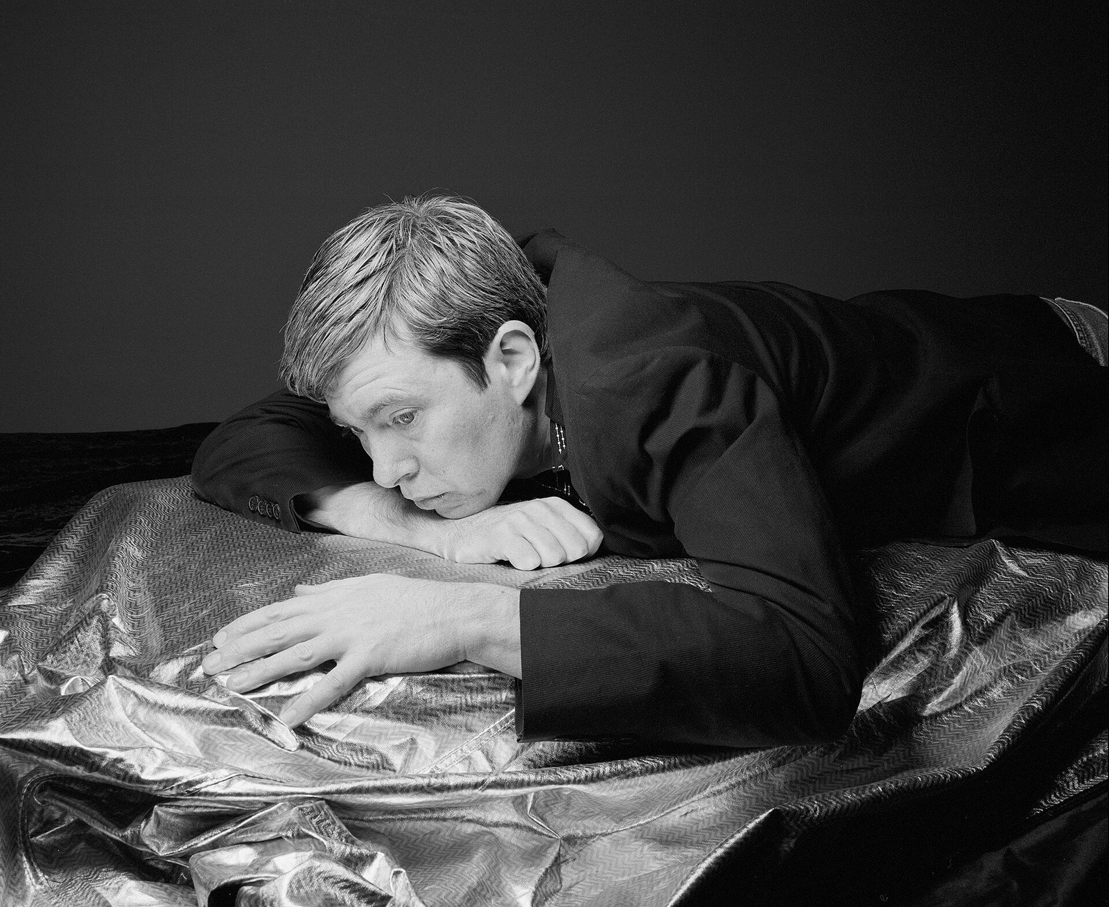 Black and white portrait of Bill Callahan lying on silver fabric, photographed by Oliver Mark in Berlin, 2011