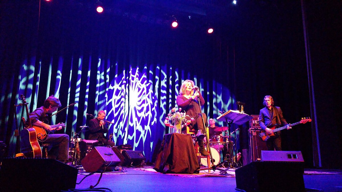 Buy Cowboy Junkies tickets on StubOrder Cowboy Junkies performing on stage, Margo Timmins singing from a stool at center, October 2015