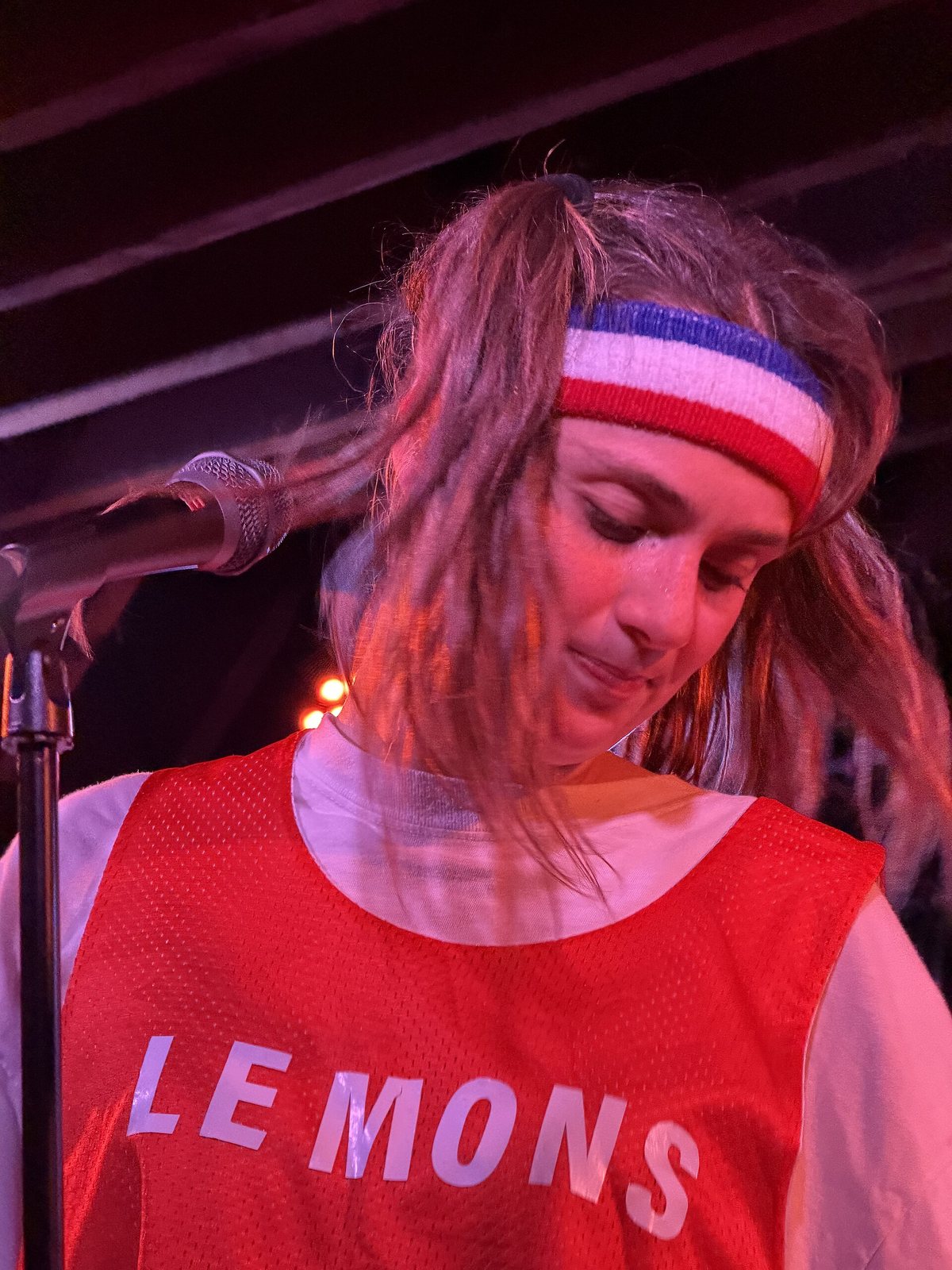 Dev Lemons performing on stage in a red 'LEMONS' mesh top and striped headband, 2026