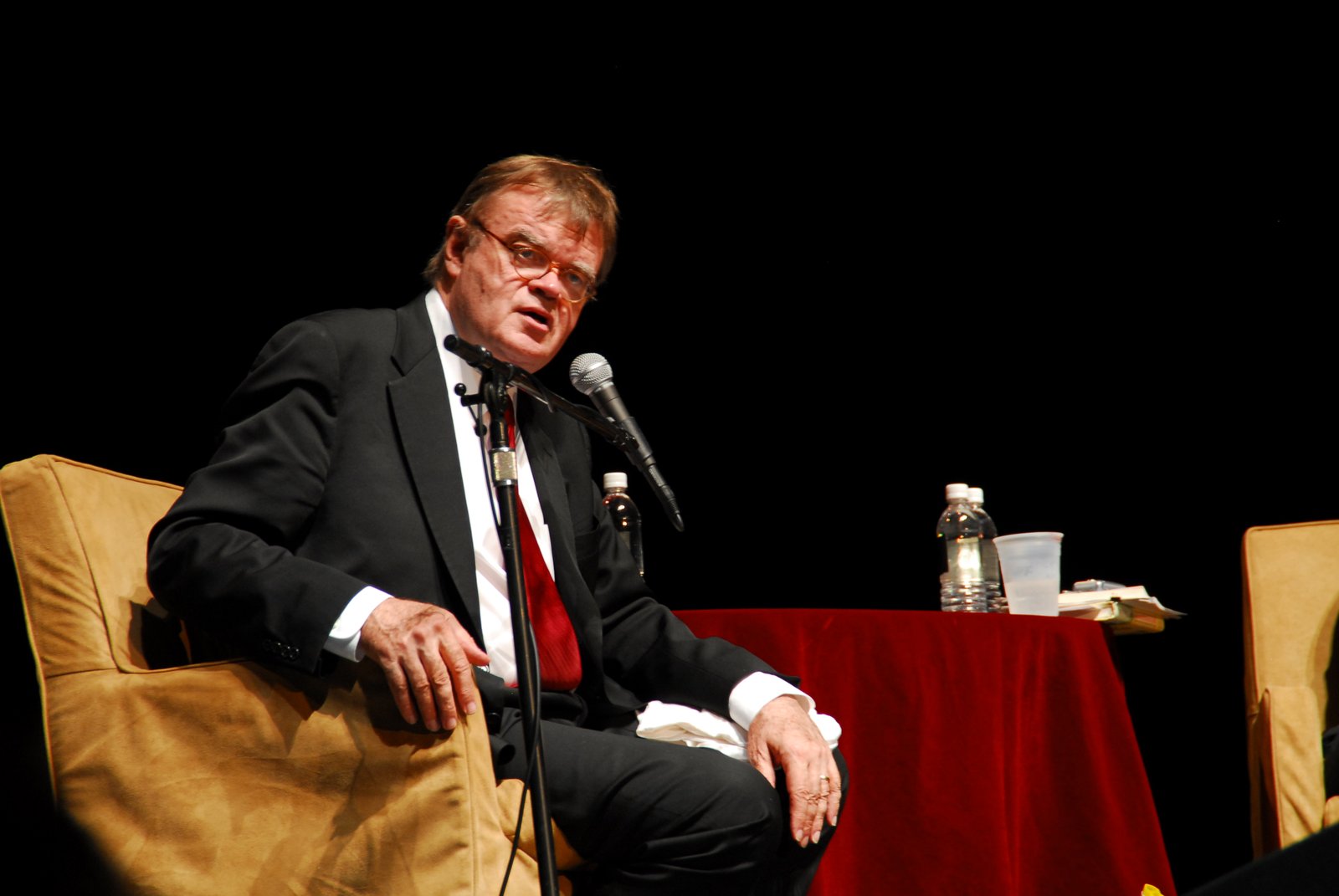 Garrison Keillor seated on stage with a microphone at the Wilshire Theatre, Los Angeles, 2007 - Garrison Keillor tickets
