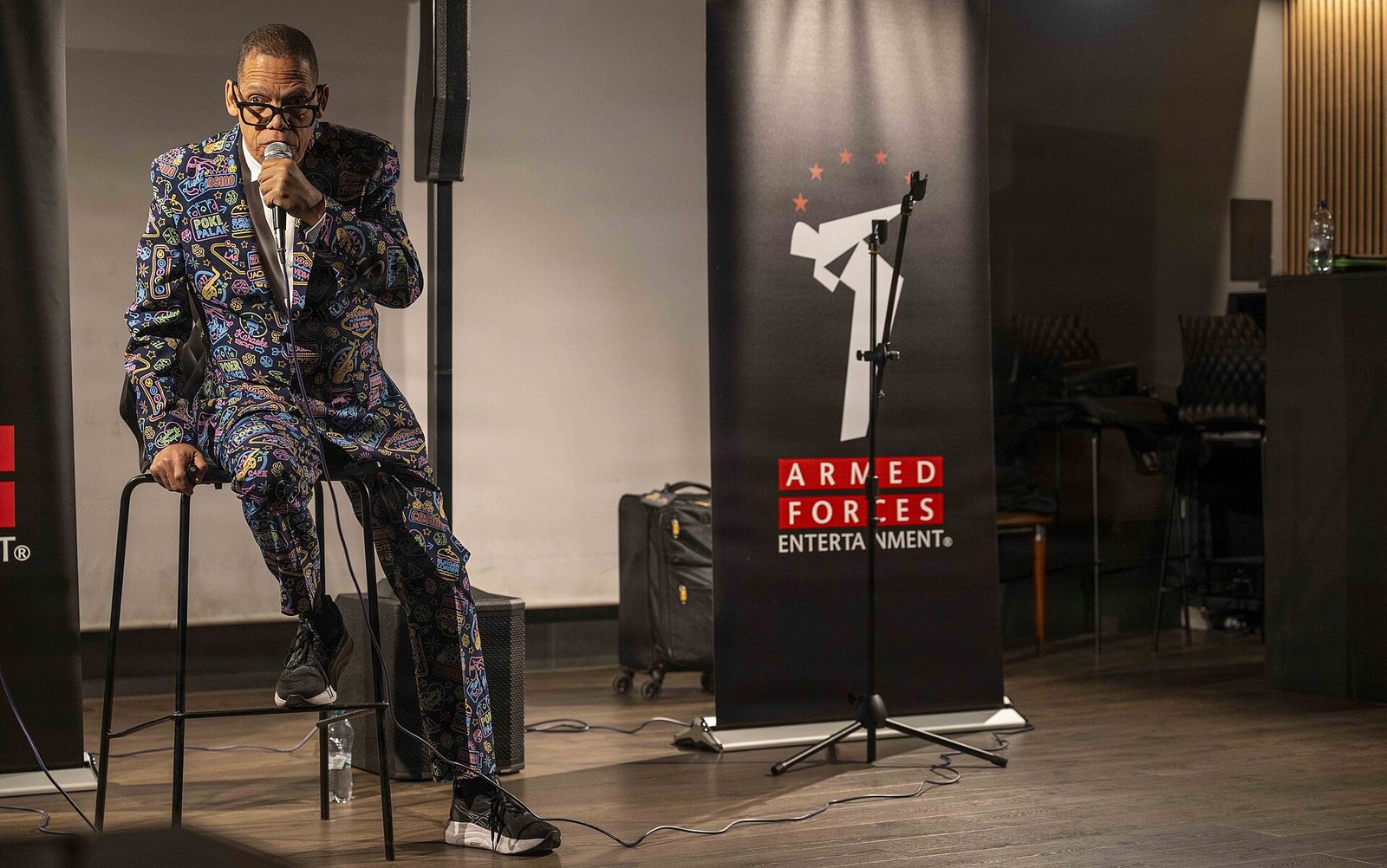 Greg Morton performing stand-up on a stool at Naval Air Station Sigonella, Italy, 2026