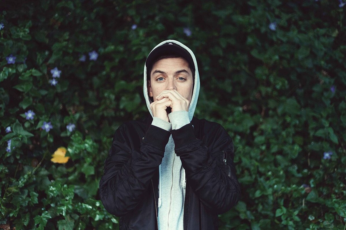 Buy Grieves tickets on StubOrder Grieves (Benjamin Laub) in a hooded jacket in front of a leafy hedge with purple flowers, Seattle, 2018