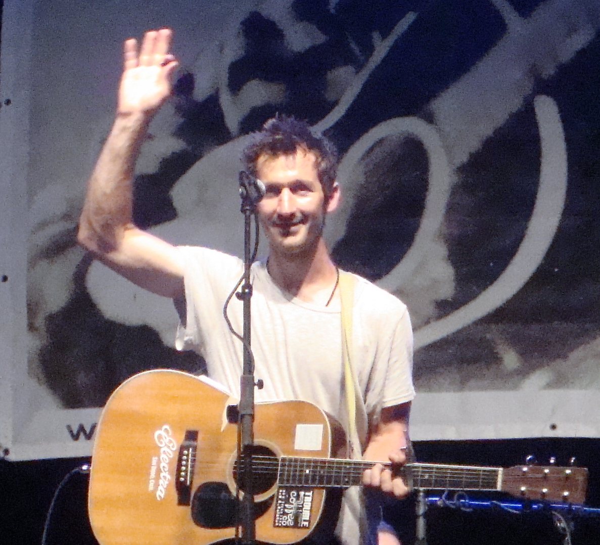 Griffin House waving on stage with an acoustic guitar at the Woody Guthrie Folk Festival, Okemah, Oklahoma, 2013