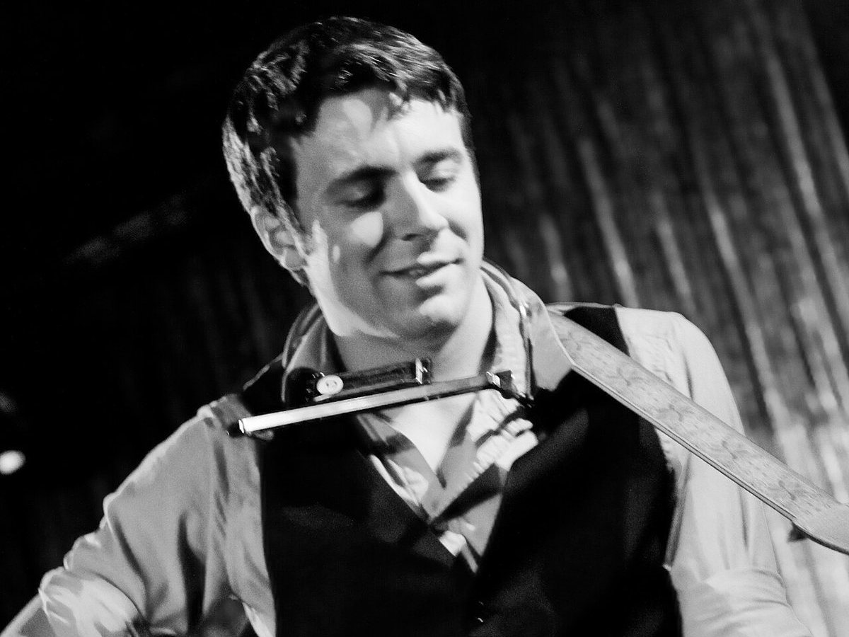 Joe Pug performing with guitar and harmonica on stage, 2011
