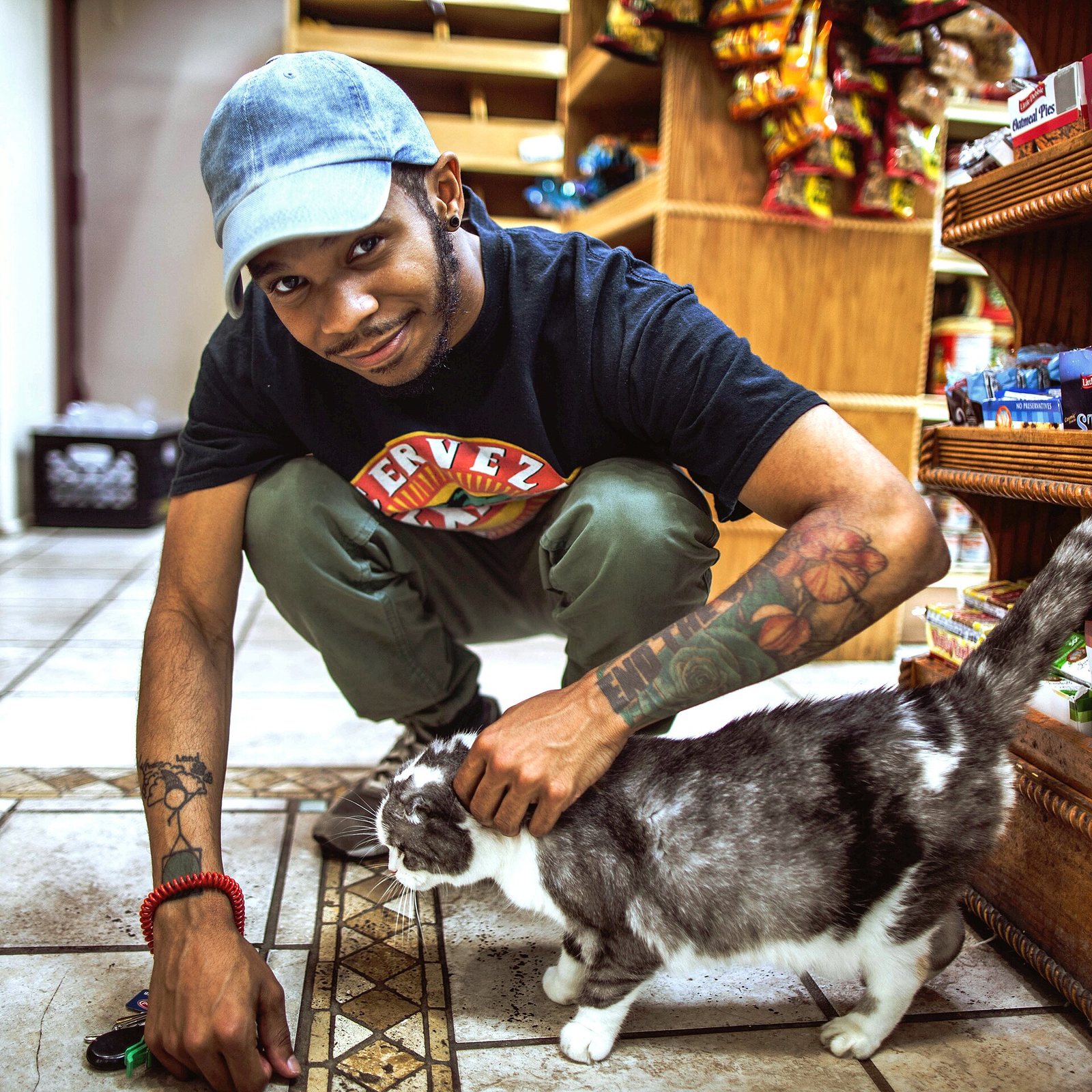 KOTA The Friend crouching to pet a cat inside a Brooklyn bodega, 2017