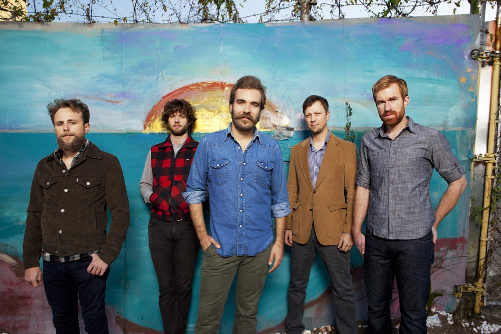 Red Wanting Blue band members posed in front of a painted mural, 2012