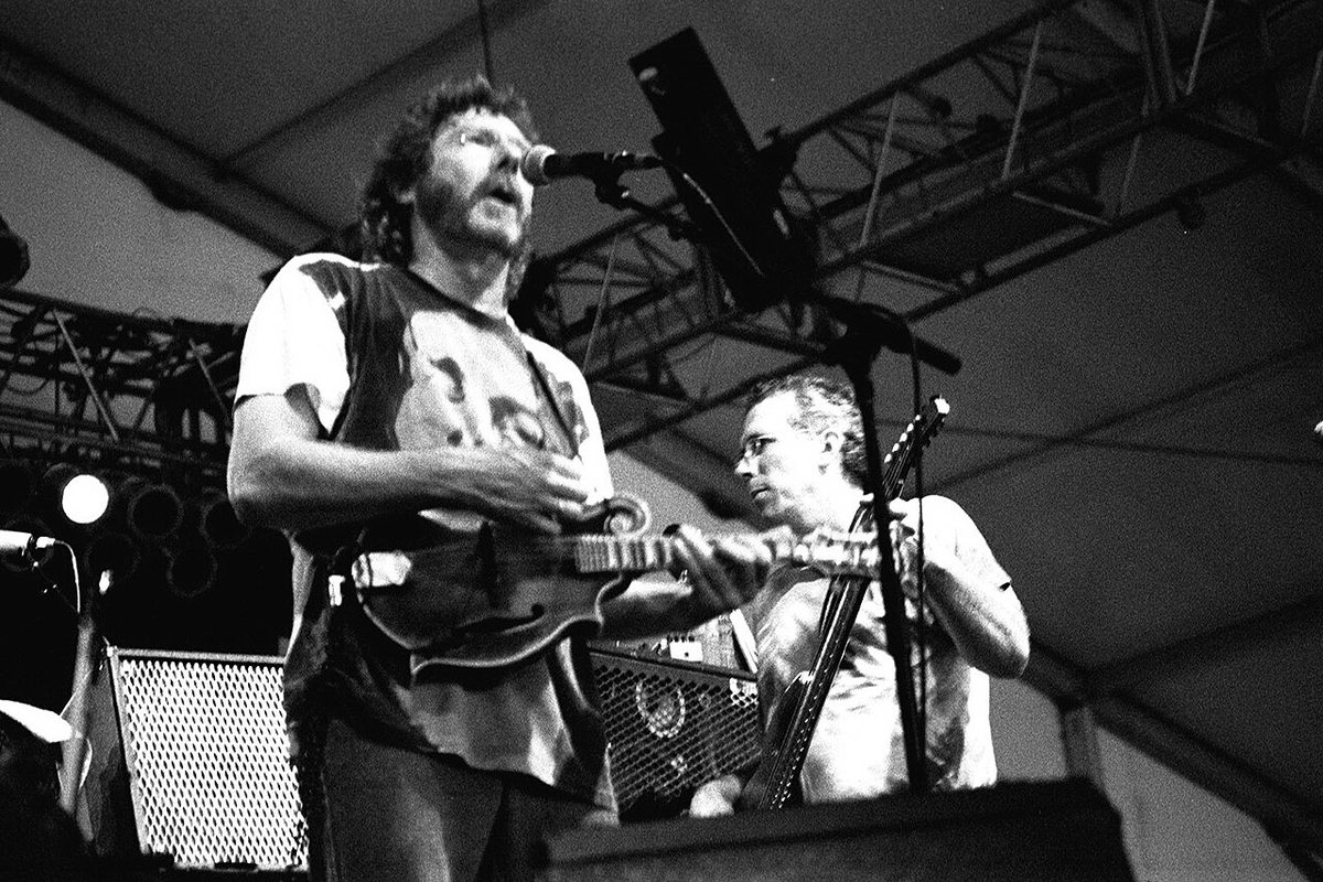 Buy Leftover Salmon, Sam Bush & Deer Creek tickets on StubOrder Black and white photo of Sam Bush singing and playing mandolin beside bassist Byron House on stage