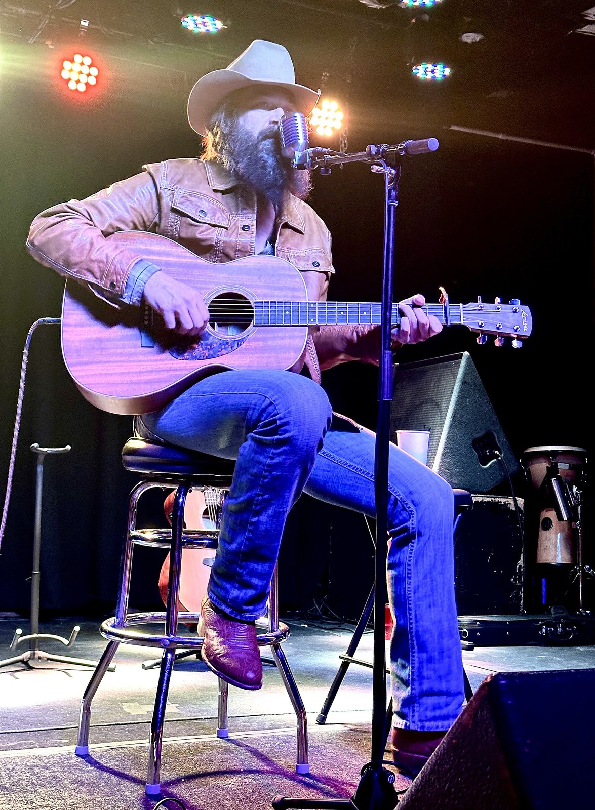 Ward Davis seated with an acoustic guitar, singing on stage at Globe Hall, Denver, 2024